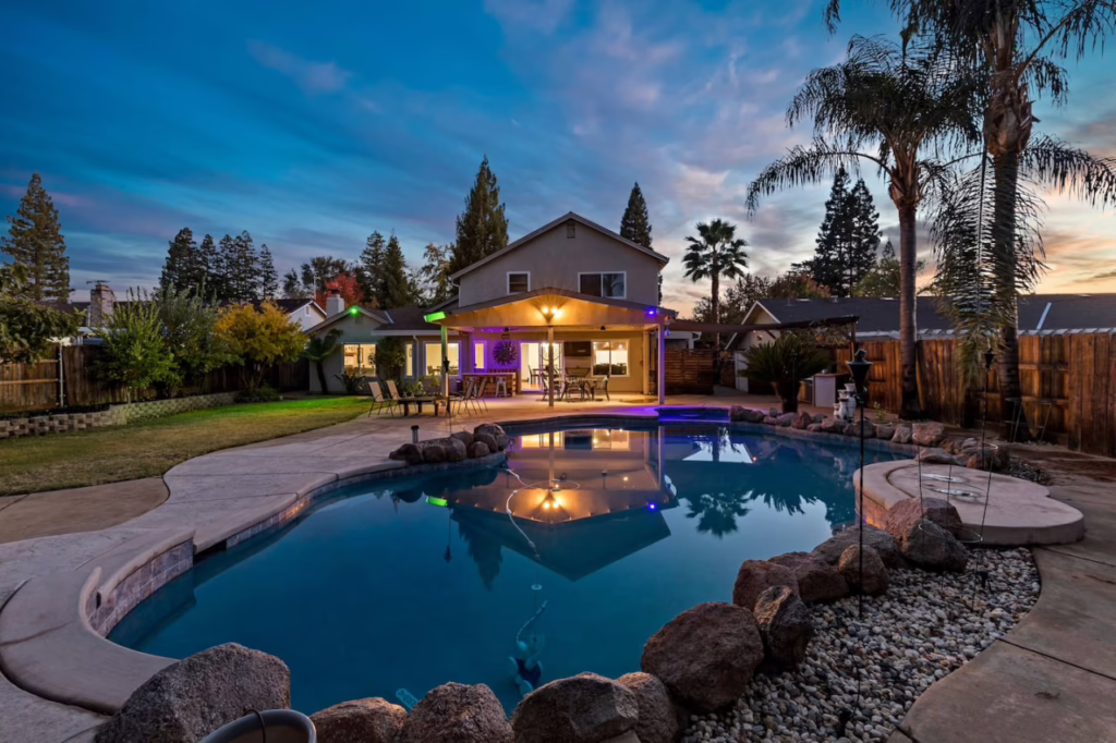 Backyard pool with gazebo and lights at sunset.